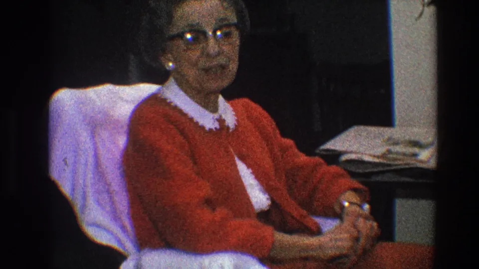 Older woman in glasses appears to speak from a chair in 1968 Toledo 8mm home-movie footage.