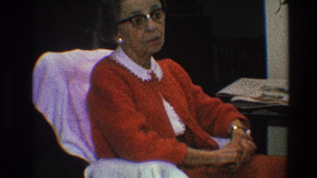 Elderly woman in eyeglasses sits in profile with hands folded in her lap.