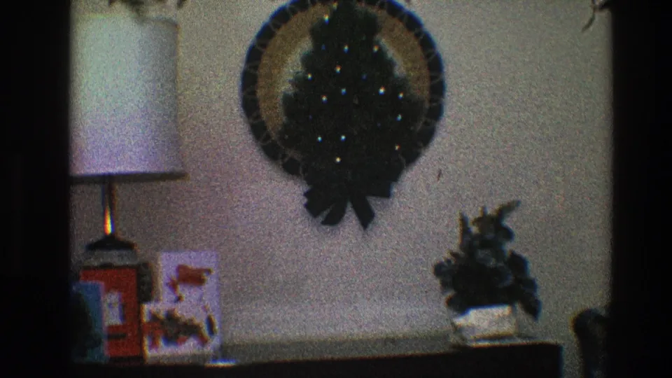 The 1968 home-movie frame shows holiday decor with a wreath, lamp, cards, and small plant in a Toledo interior.