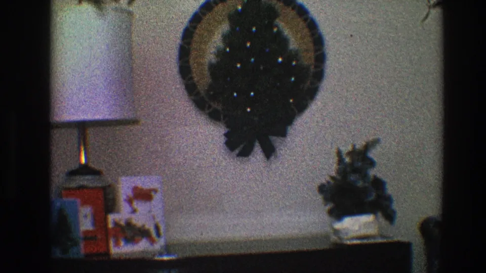 A softly exposed 8mm frame records a wreath, lamp, cards, and small plant in a 1968 Toledo home interior.