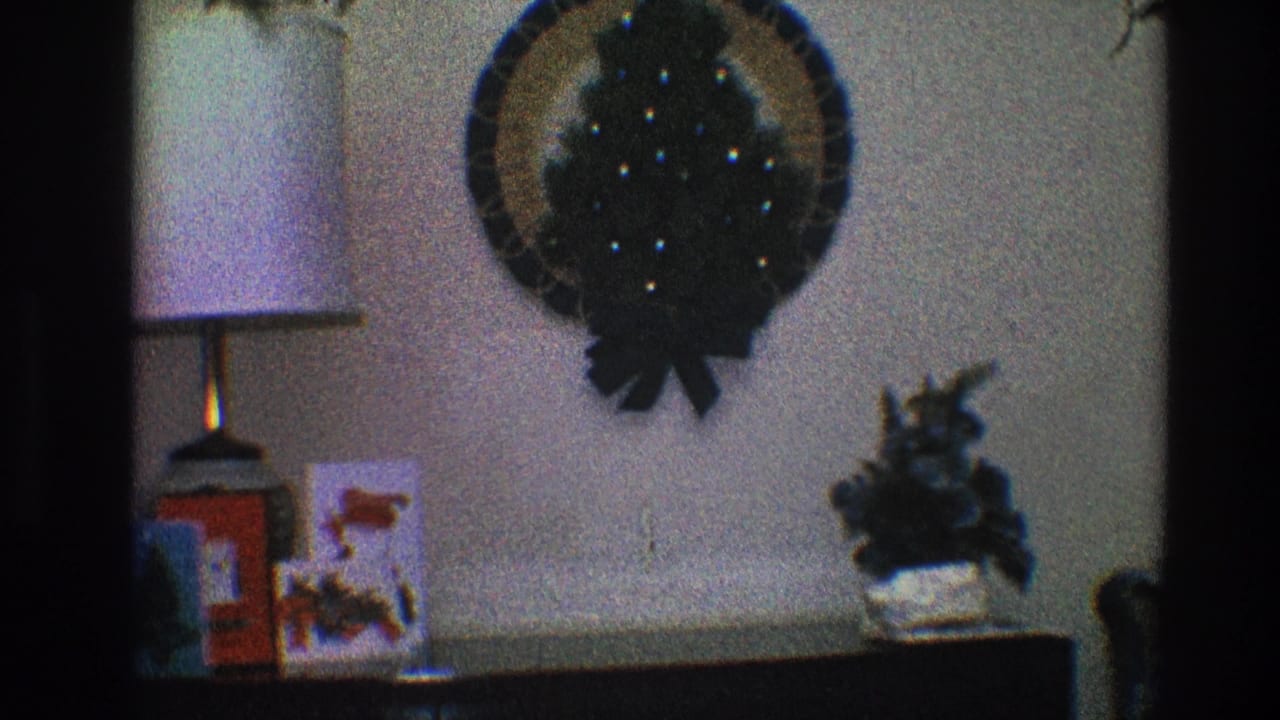 Living room wall with Christmas wreath, lamp, holiday card, red box, and potted plant.
