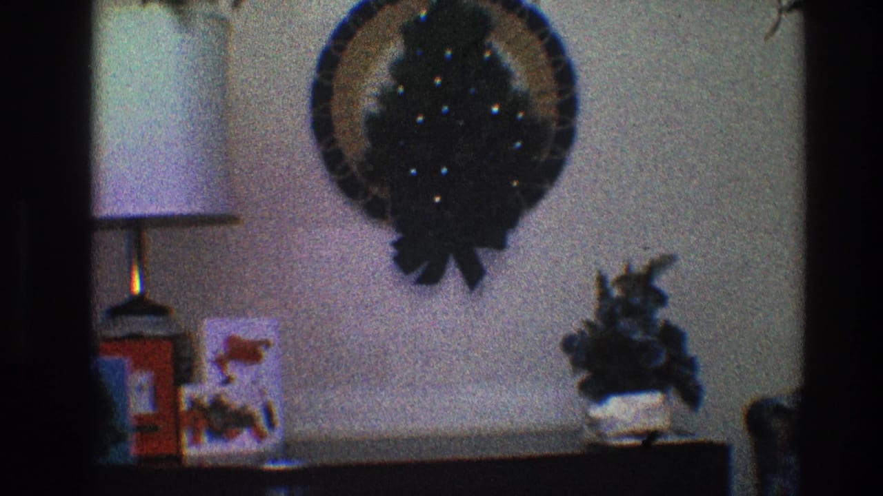 Christmas wreath above a lamp, red box, holiday card, and plant on a dark surface.