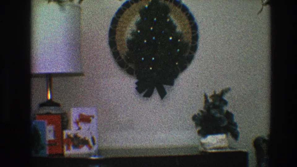 Home-movie frame from 1968 Toledo showing holiday decor on a wall and tabletop, with film grain and soft exposure.