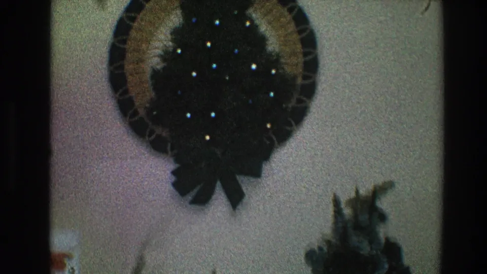 Closer 1968 Toledo home interior view of a circular Christmas wreath with small tree and bow, with a plant near the lower right.