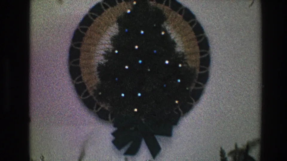 1968 Toledo home-movie frame showing a circular lit Christmas wreath with a dark green tree-shaped center and bow.