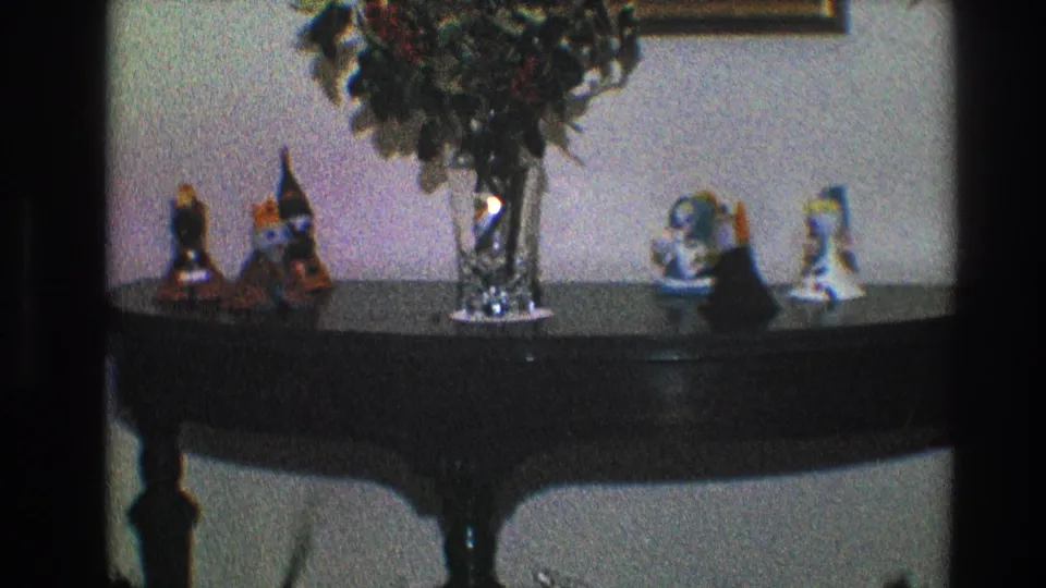 1968 Toledo home-movie frame showing a dark wood console table with a crystal vase, greenery, and decorative figurines.