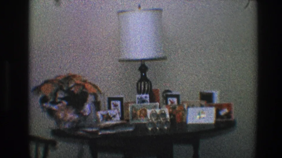 1968 Toledo living-room detail with a lamp centered above framed photographs and small decorative objects on a table.