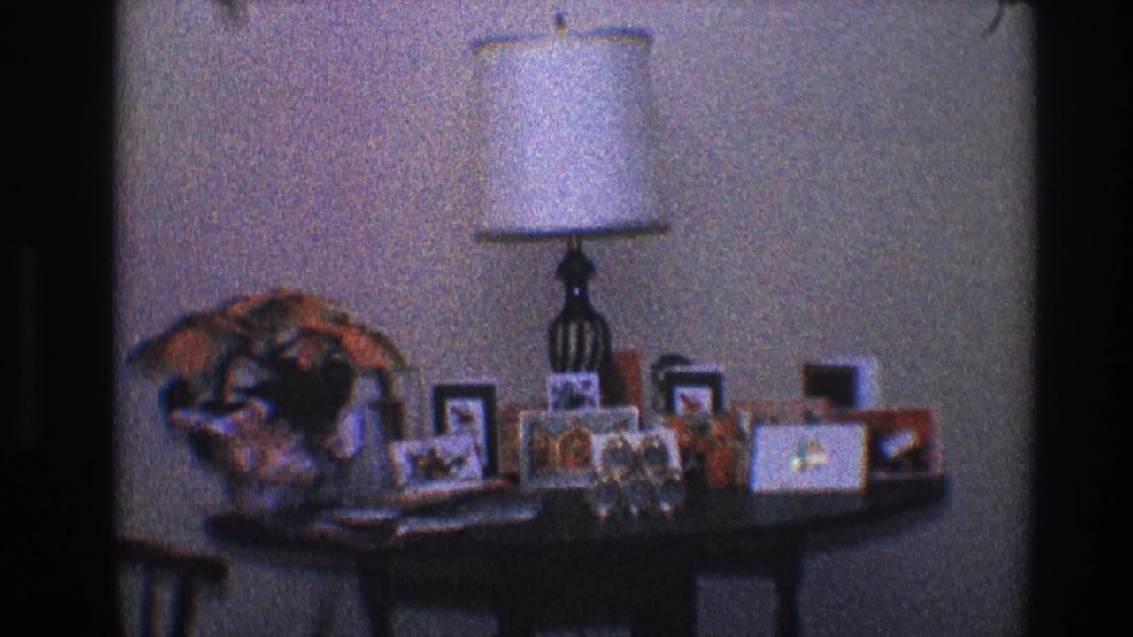 Dark wooden table with a white lamp, framed photos, and a decorative arrangement against a wall.