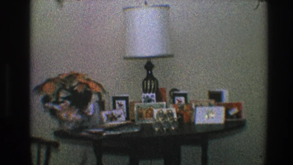 Static 8mm view of a Toledo, Ohio interior with a lamp, photo frames, decorative arrangement, and tabletop keepsakes.