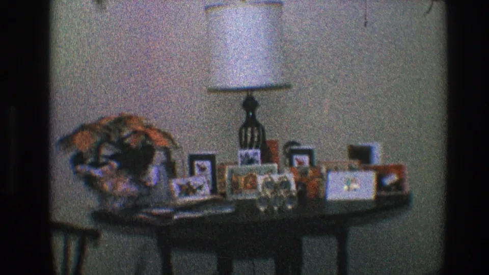 Toledo, Ohio 1968 8mm frame with a white-shaded lamp, family photo frames, and decorative keepsakes on a dark wooden table.