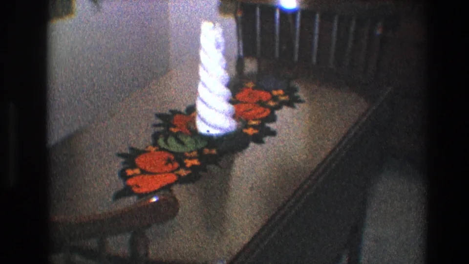 Grainy 1968 Toledo home-movie frame showing the white spiral candle on the red and green runner across the dinette table.