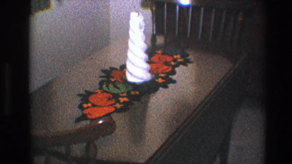 1968 Toledo interior detail with a white candle, orange floral crochet runner, and wood table seen in grainy 8mm footage.