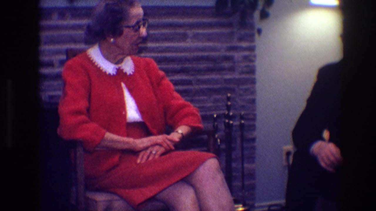 Woman in a red dress sits in a chair beside a stone fireplace.