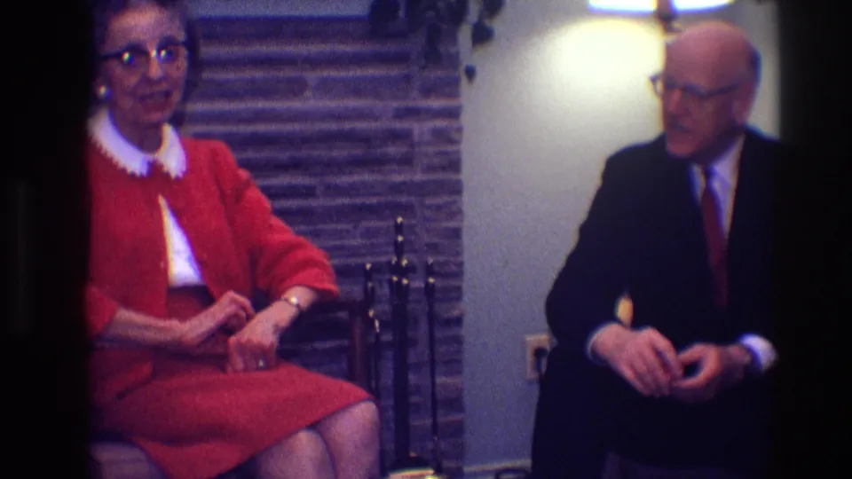 The seated pair face one another in a 1968 Toledo interior, with the fireplace tools and stone hearth behind them.