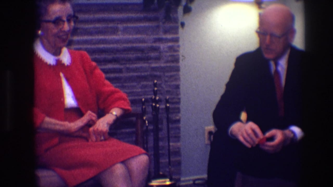 Woman in red dress and suited man sit facing one another indoors.