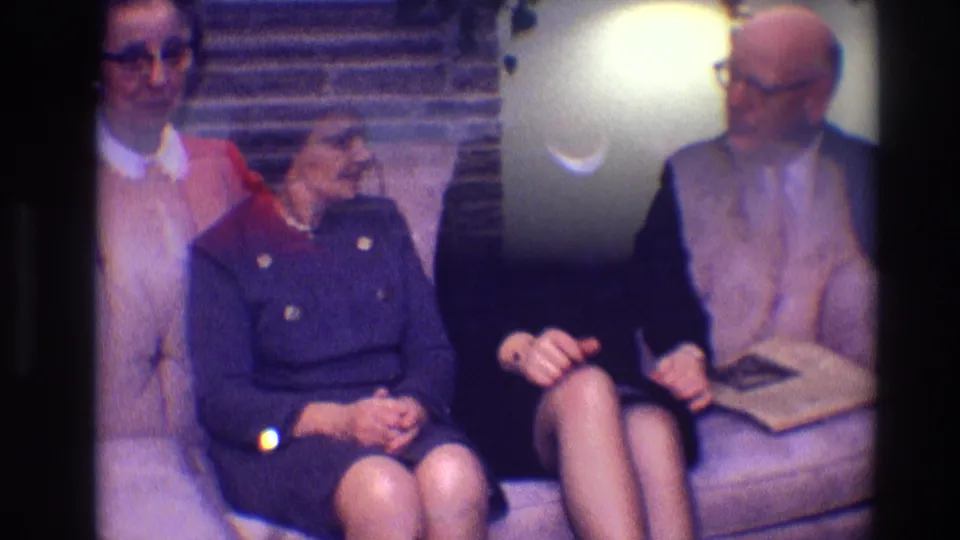 1968 Toledo home-movie frame showing an older woman and younger woman seated together on a couch in a living room.
