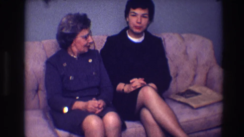 The two adult women continue their seated conversation on a brown sofa in supported 1968 Toledo home-movie footage.