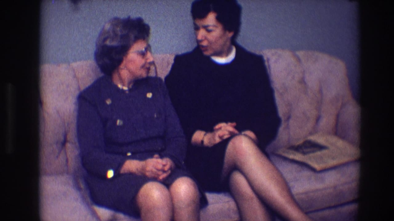 Two women sit on a tan sofa, turned slightly toward one another in conversation.