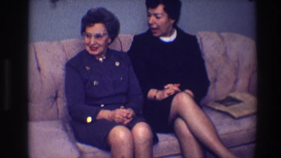 A 1968 Toledo frame shows two women seated together on a tan sofa, with the older woman turned slightly toward the camera.