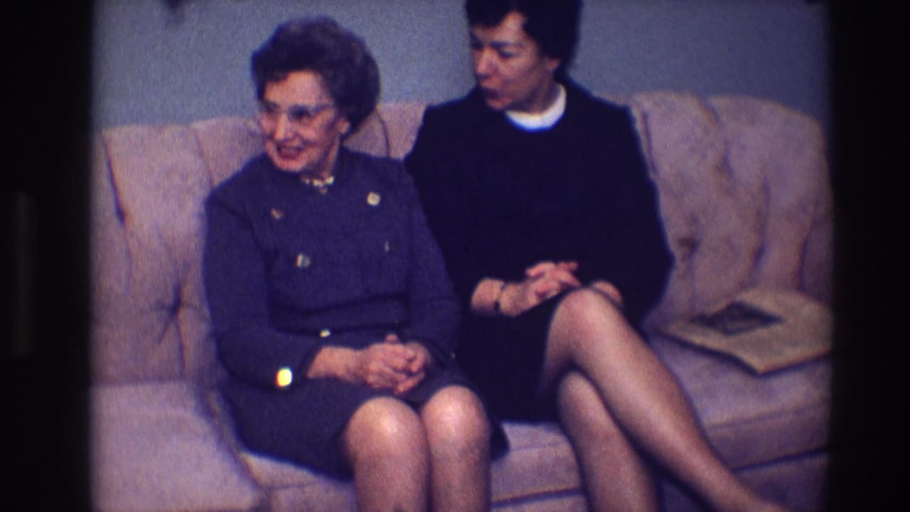 Two women seated on a light-colored couch, with the older woman smiling toward the left.