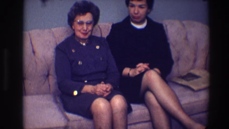 1968 Toledo home-movie frame of two women seated on a couch, one facing forward and one looking downward.