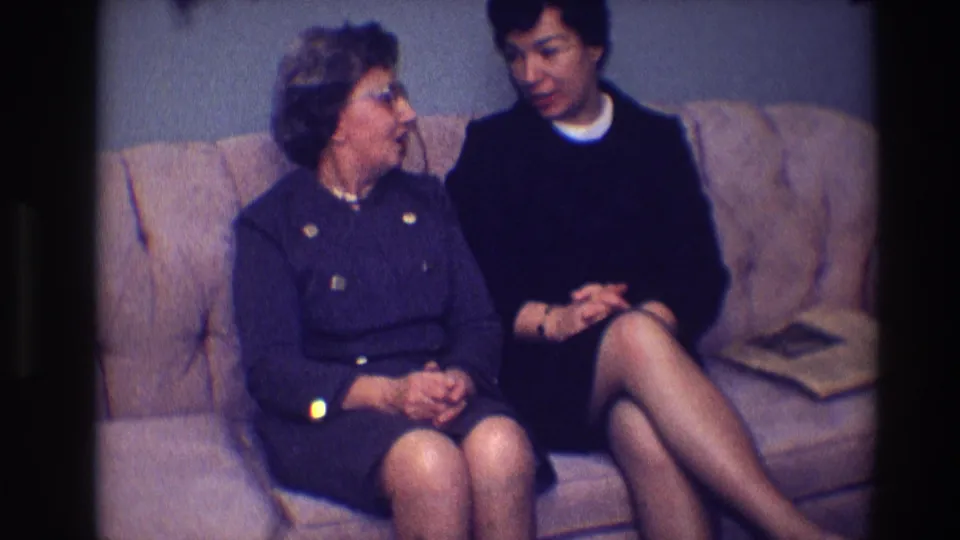1968 Toledo home-movie frame showing an older woman turned toward a younger woman during a couch conversation.