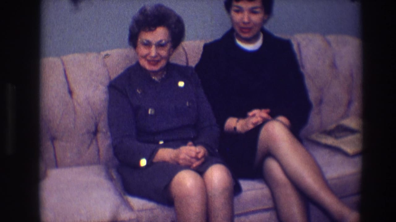 Older woman in a blue suit smiles beside a younger woman in a black dress.