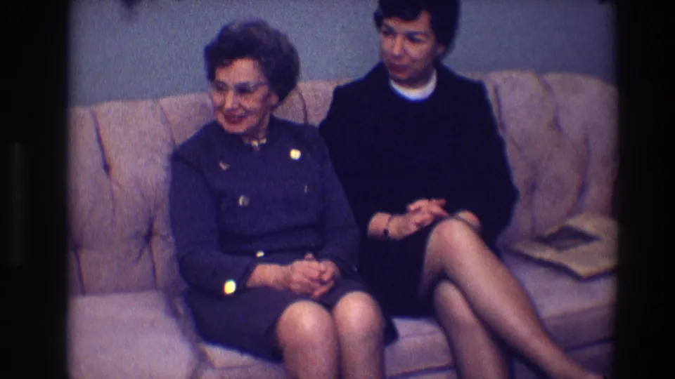 In this 1968 Toledo interior frame, two women on a tan sofa turn their attention off camera during conversation.