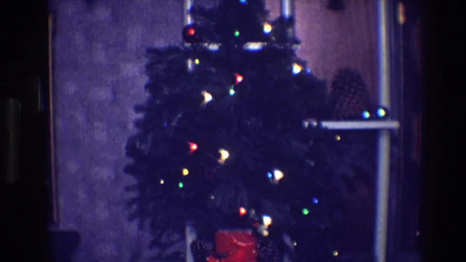 1968 Toledo home-movie frame of a dark green Christmas tree with multicolored lights in a dim interior.