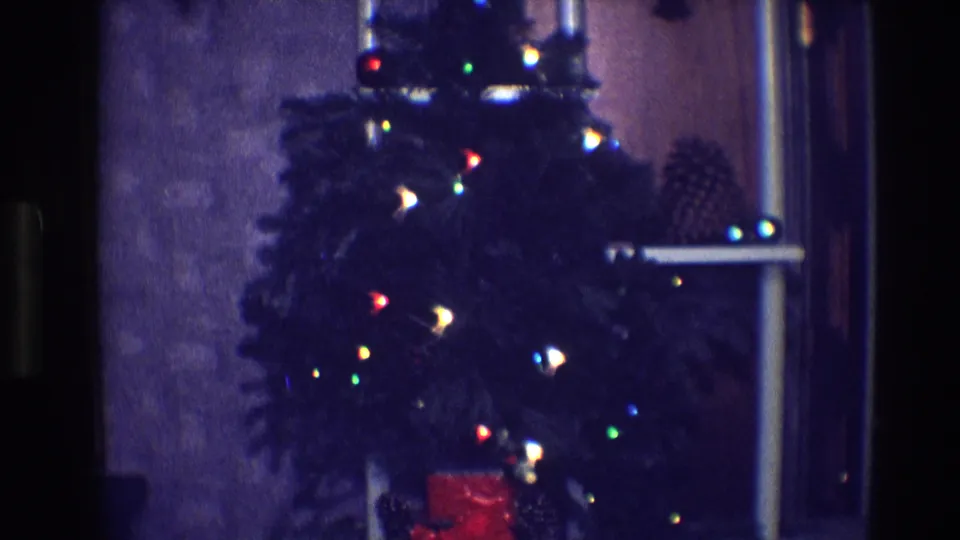 1968 Toledo home-movie still of a decorated indoor Christmas tree with glowing lights and a red box beneath it.