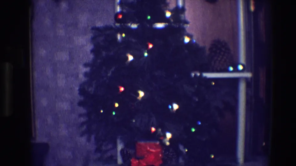 Late-1960s 8mm frame from Toledo showing a glowing Christmas tree in a subdued indoor holiday setting.