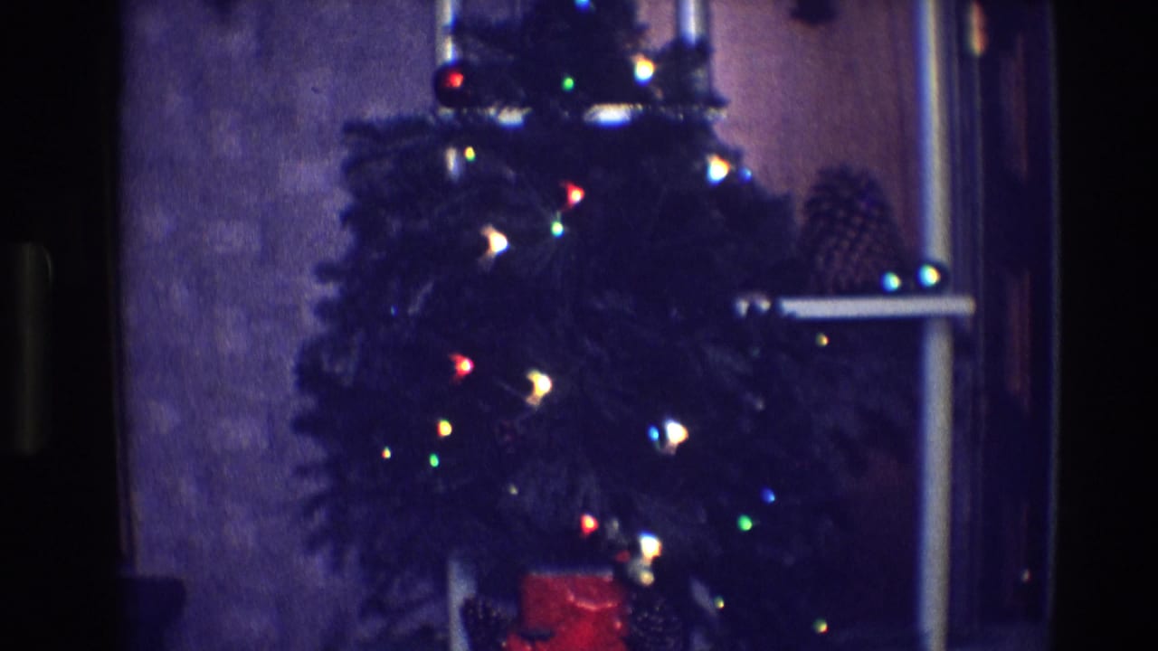 Small Christmas tree with glowing colored lights beside a window.