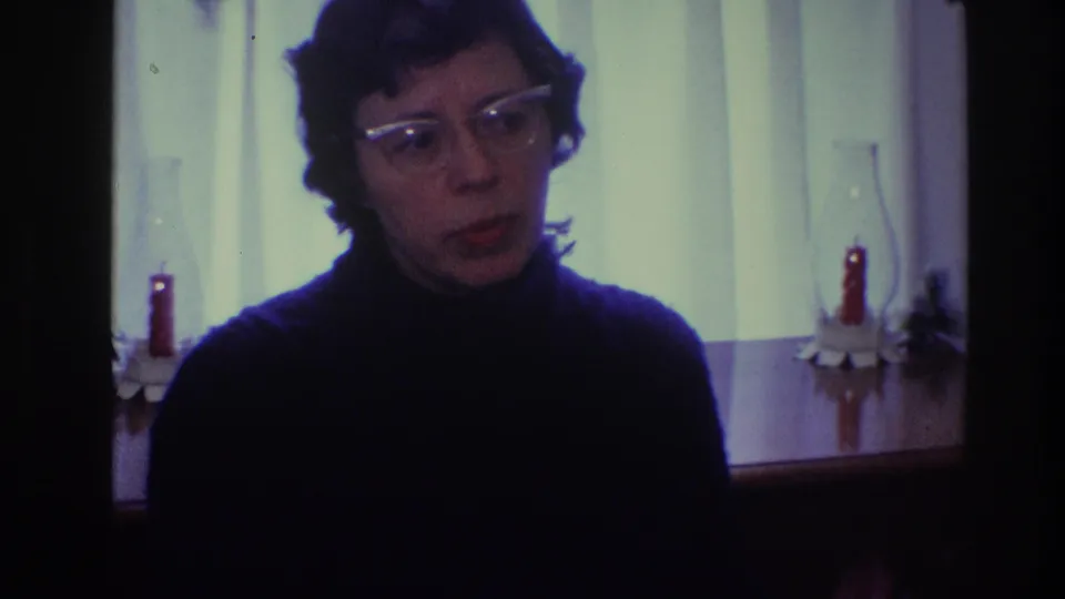 The 1968 Toledo 8mm frame shows a woman with glasses addressing the camera from a close domestic setting.