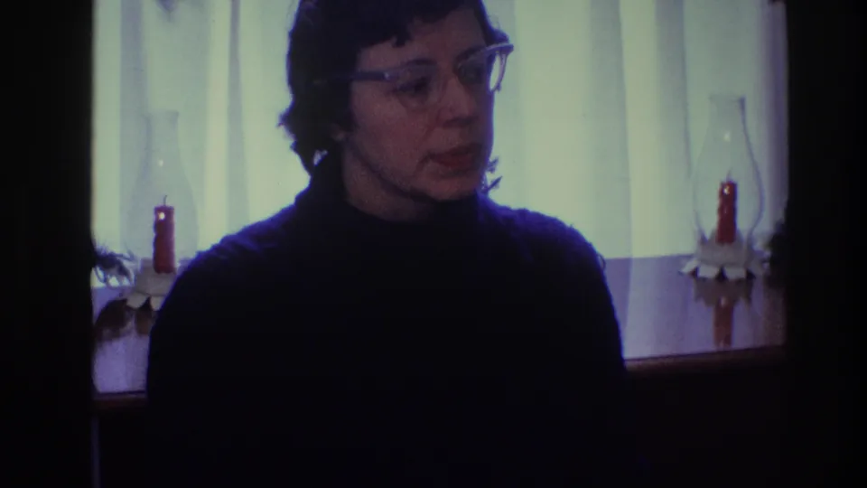 In Toledo, Ohio 1968 home-movie footage, a woman in glasses and a dark turtleneck looks off-camera in a softly lit room.