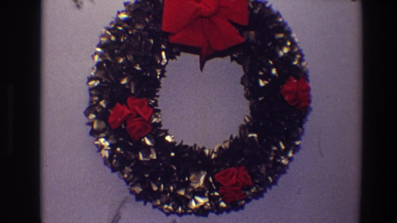 Black tinsel wreath with red bows hanging on a pale interior wall.