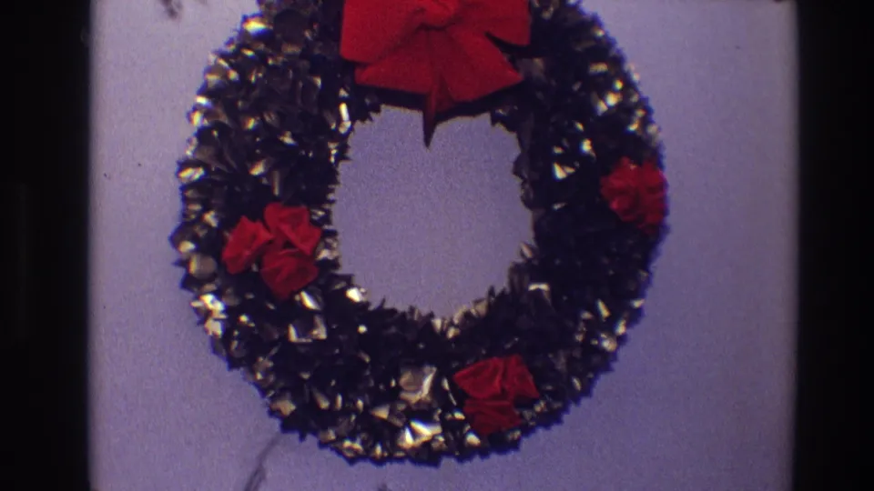 1968 Toledo frame holding on the Christmas wreath, with metallic dark tinsel, red bow and fabric flowers visible in soft 8mm color.