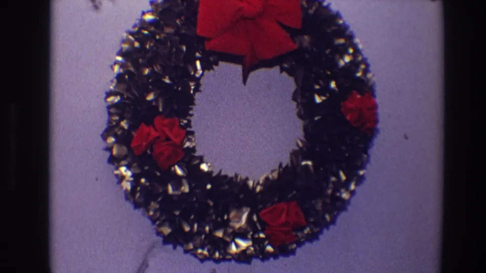 1968 Toledo home-movie close-up of a Christmas wreath, cropped tightly around shiny dark tinsel, red fabric flowers and a red bow.