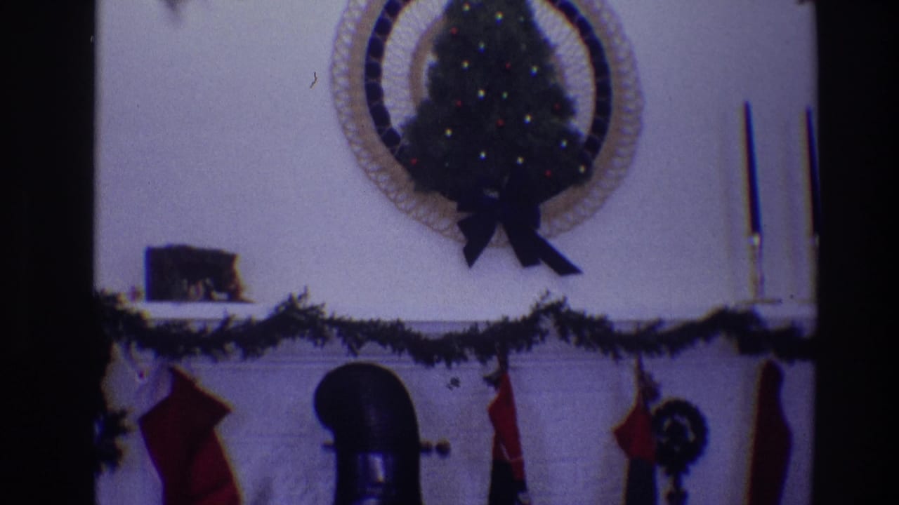 Christmas mantel with garland, red stockings, small lit tree, candles, and black chimney pipe.