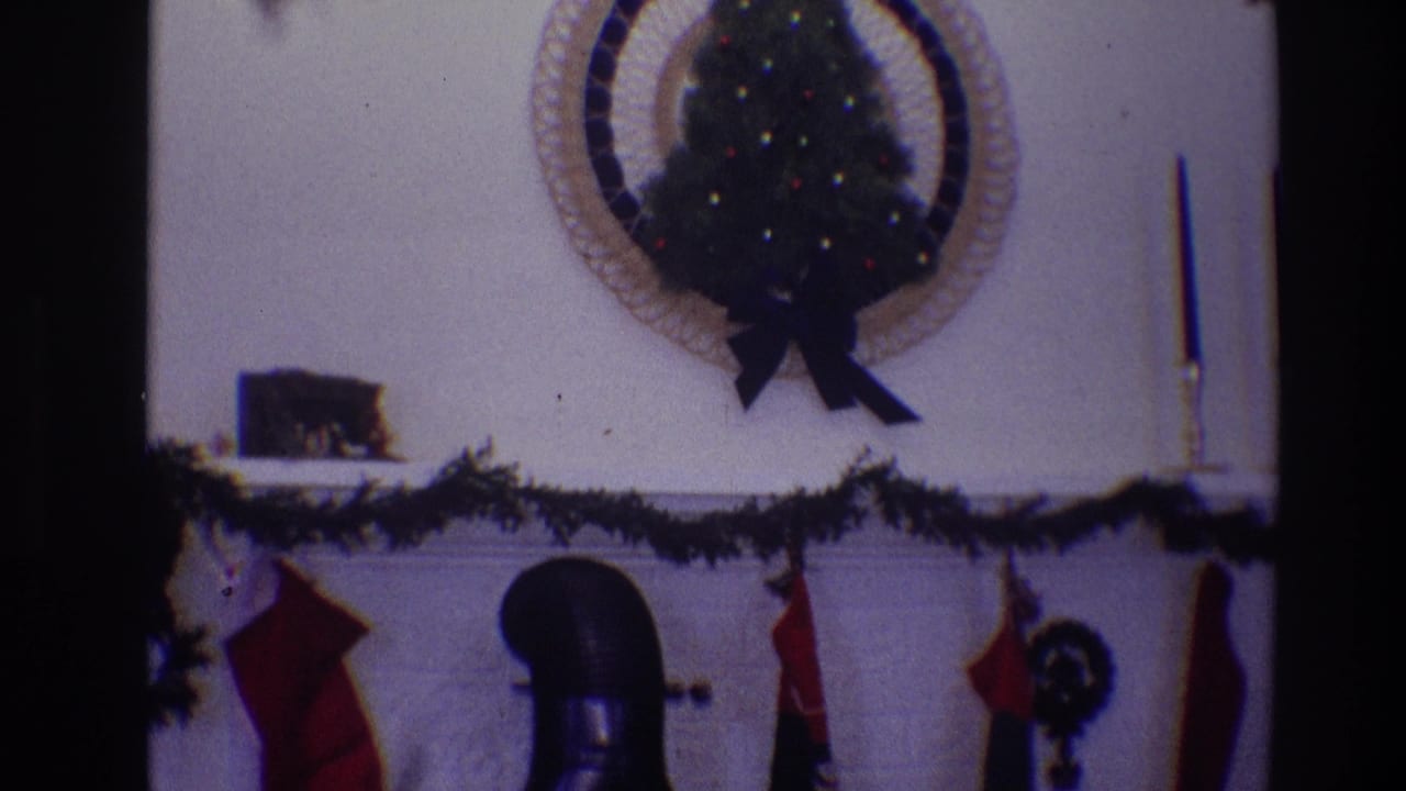 Christmas mantel with garland, stockings, small wall tree, candlestick, and black chimney pipe.
