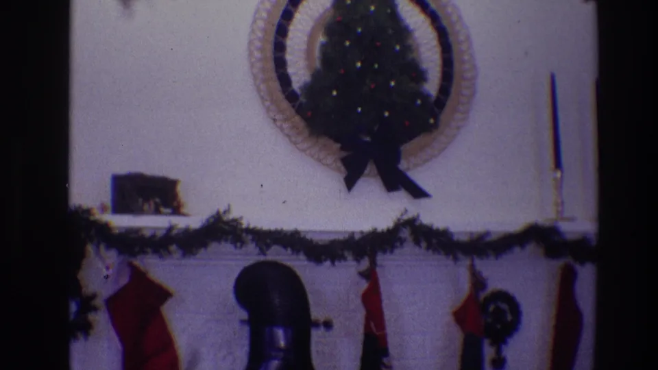 1968 Toledo home-movie frame of a Christmas mantel with stockings, garland, a small decorated wall tree, candlestick, and chimney pipe.