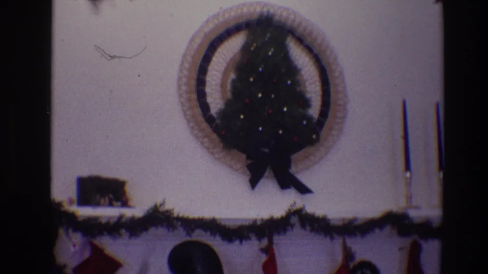 1968 Toledo frame centered on a small decorated Christmas tree above a white mantel with garland, stockings, candlesticks, and chimney pipe.
