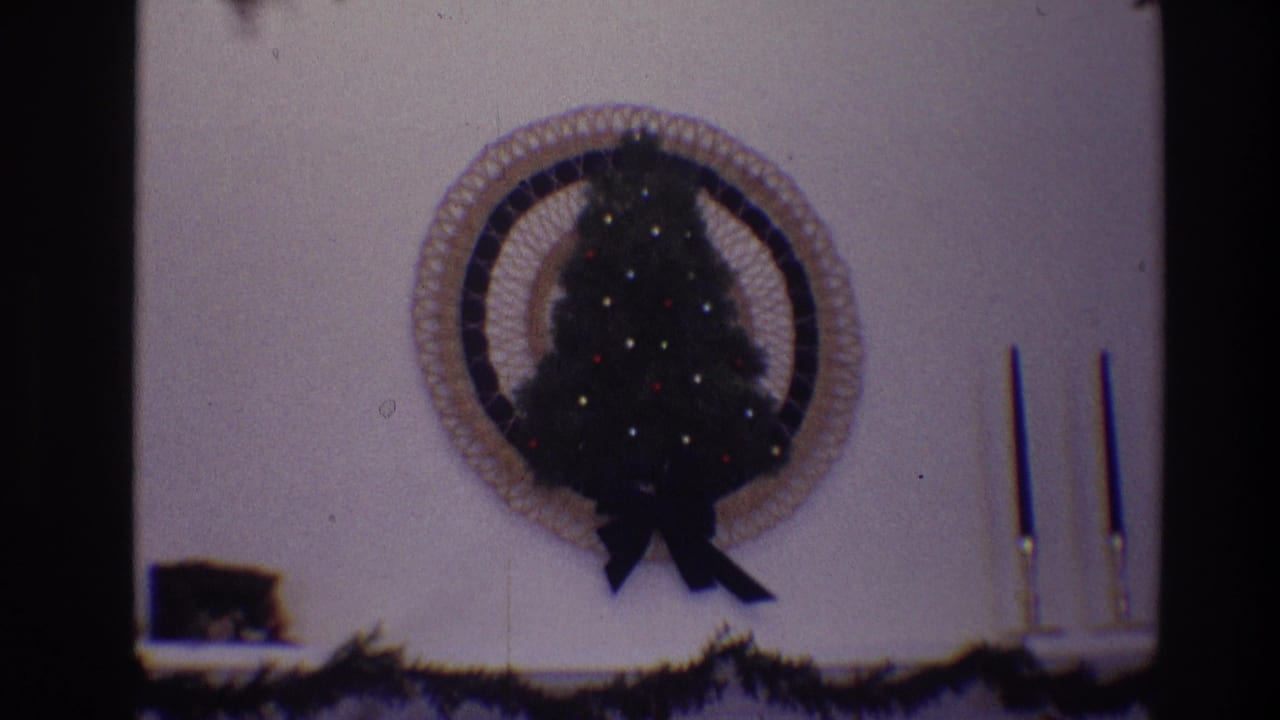 Small decorated Christmas tree mounted inside a circular wall frame above garland and candlesticks.