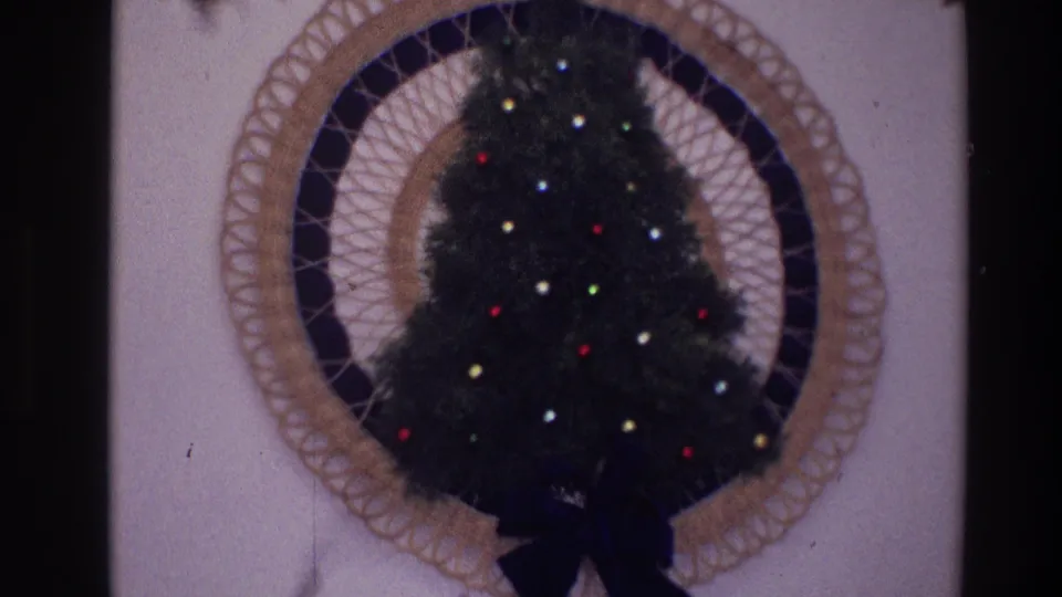 1968 Toledo home-movie close-up of the wall-mounted Christmas tree, showing colored bulbs, woven frame, and dark ribbon bow.