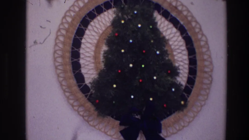 Final 1968 Toledo frame holds on the lighted wall Christmas tree inside the circular woven frame against a plain interior wall.