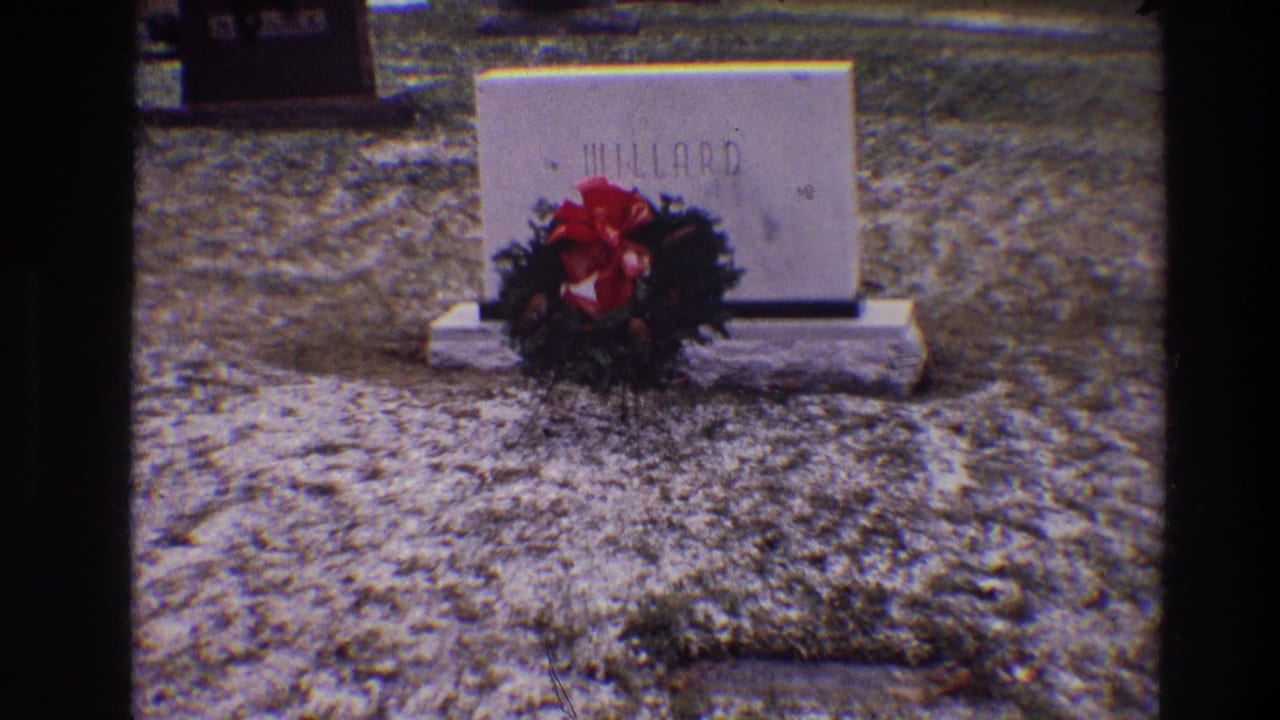 Grave marker reading Millard with a red-bowed Christmas wreath in front.
