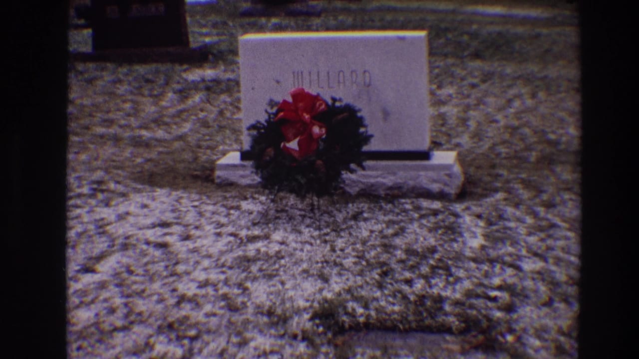 Millard grave marker and wreath centered on gravel in a cemetery setting.