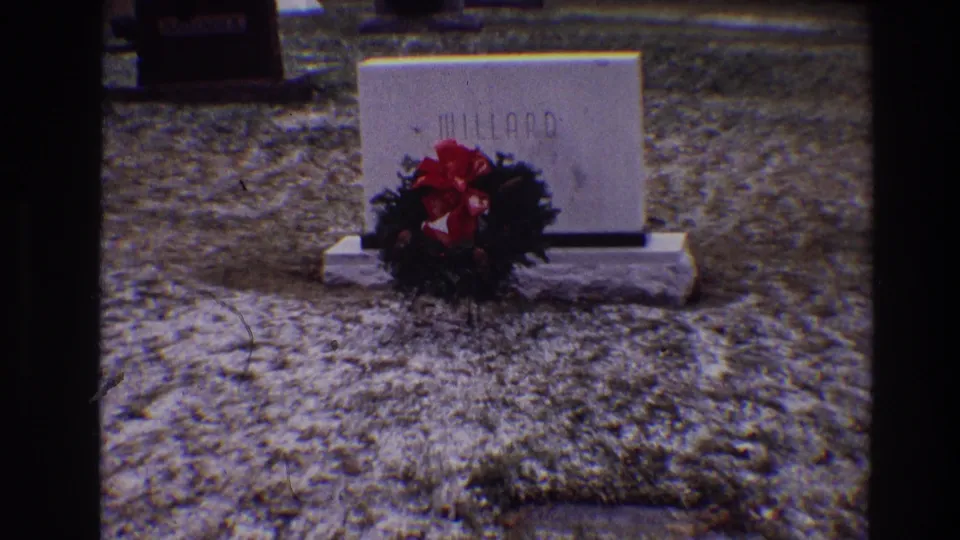 Home-movie frame from the 1968 Toledo clip showing a grave marker for Millard with a red-bowed wreath in front.