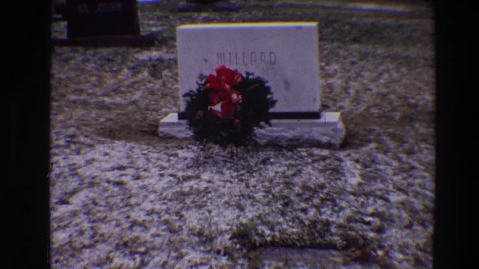 Final frame of the Toledo 1968 cemetery shot, with the Millard marker, wreath, and textured 8mm film grain visible.