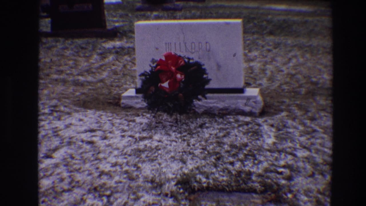 White MILLARD grave marker with a red-bowed wreath on icy grass.