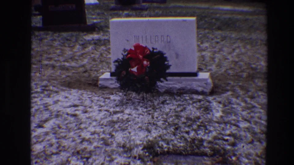 1968 Toledo 8mm frame showing a white MILLARD headstone with a green wreath and red bow at its base in a cemetery.